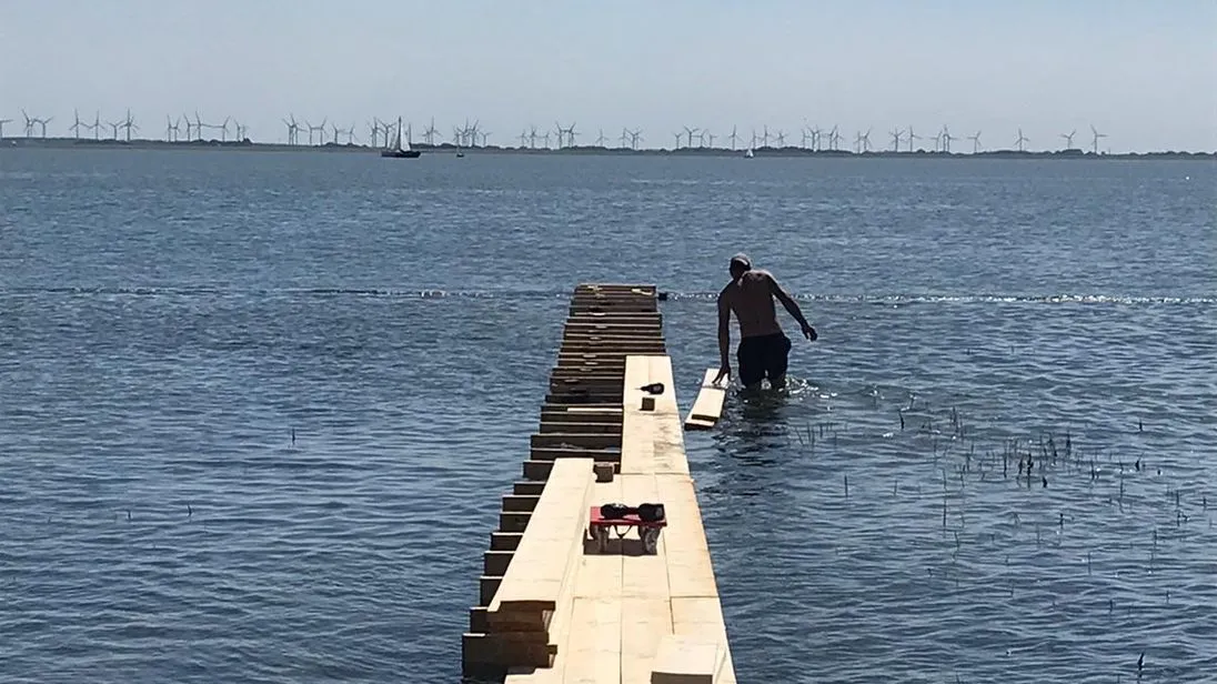 Die Aufbauarbeiten vom Steg in kurzer Hose im Wasser und mit Akkuschrauber.